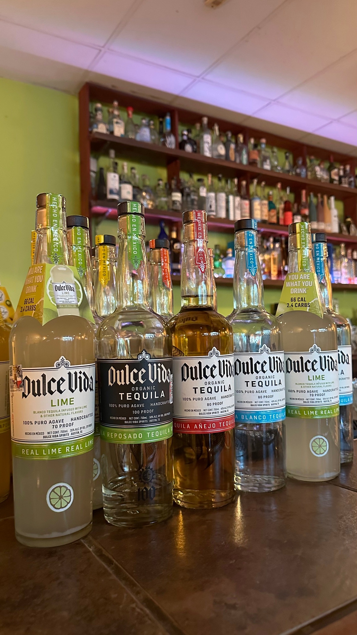 Bottles of Dulce Vida tequila and lime spirits on a bar.