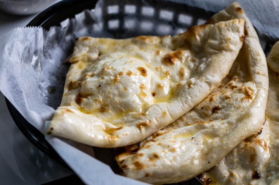 Golden-brown naan bread pieces brushed with butter in a basket.