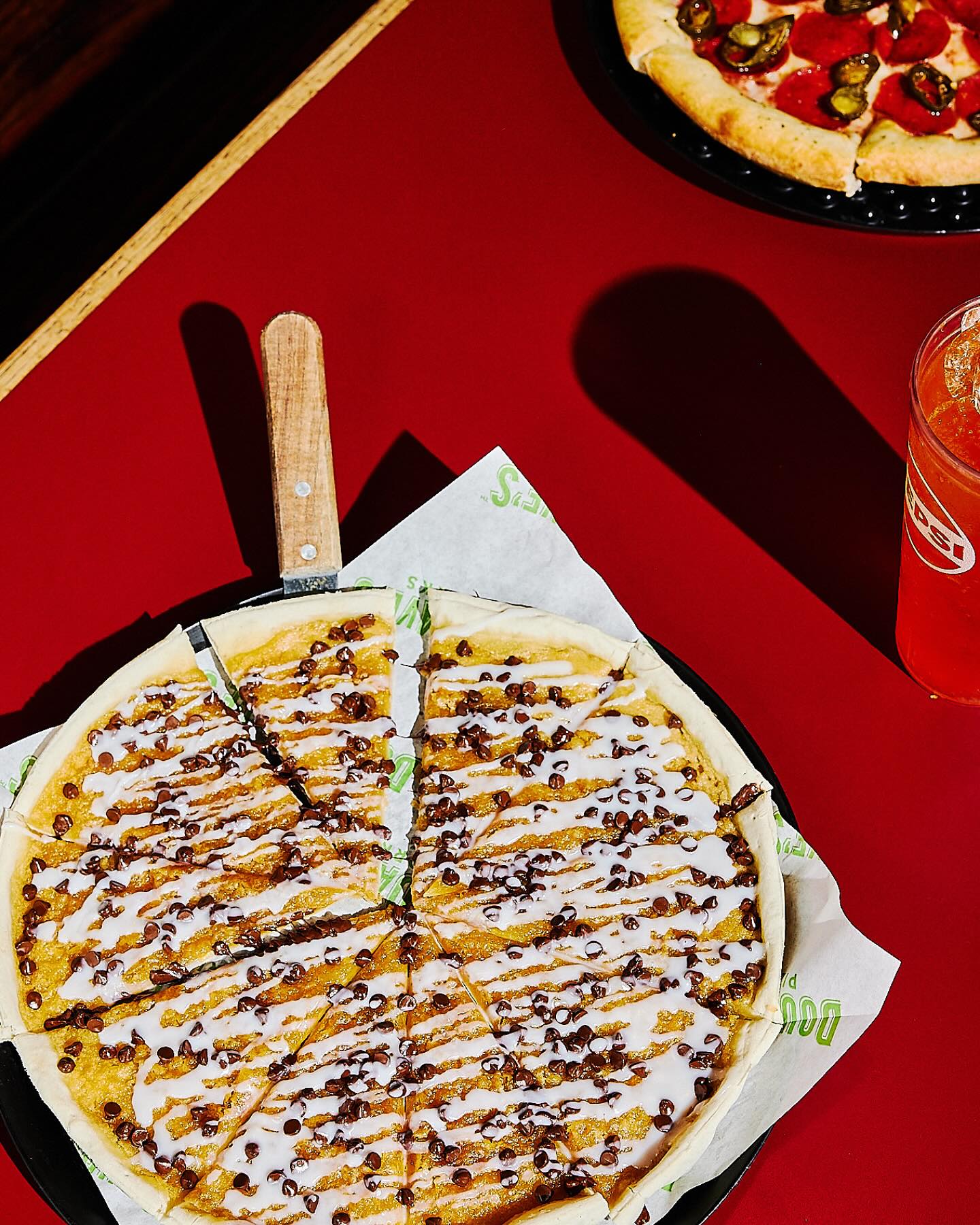 Sliced dessert pizza with white frosting, chocolate chips, and pizza cutter.