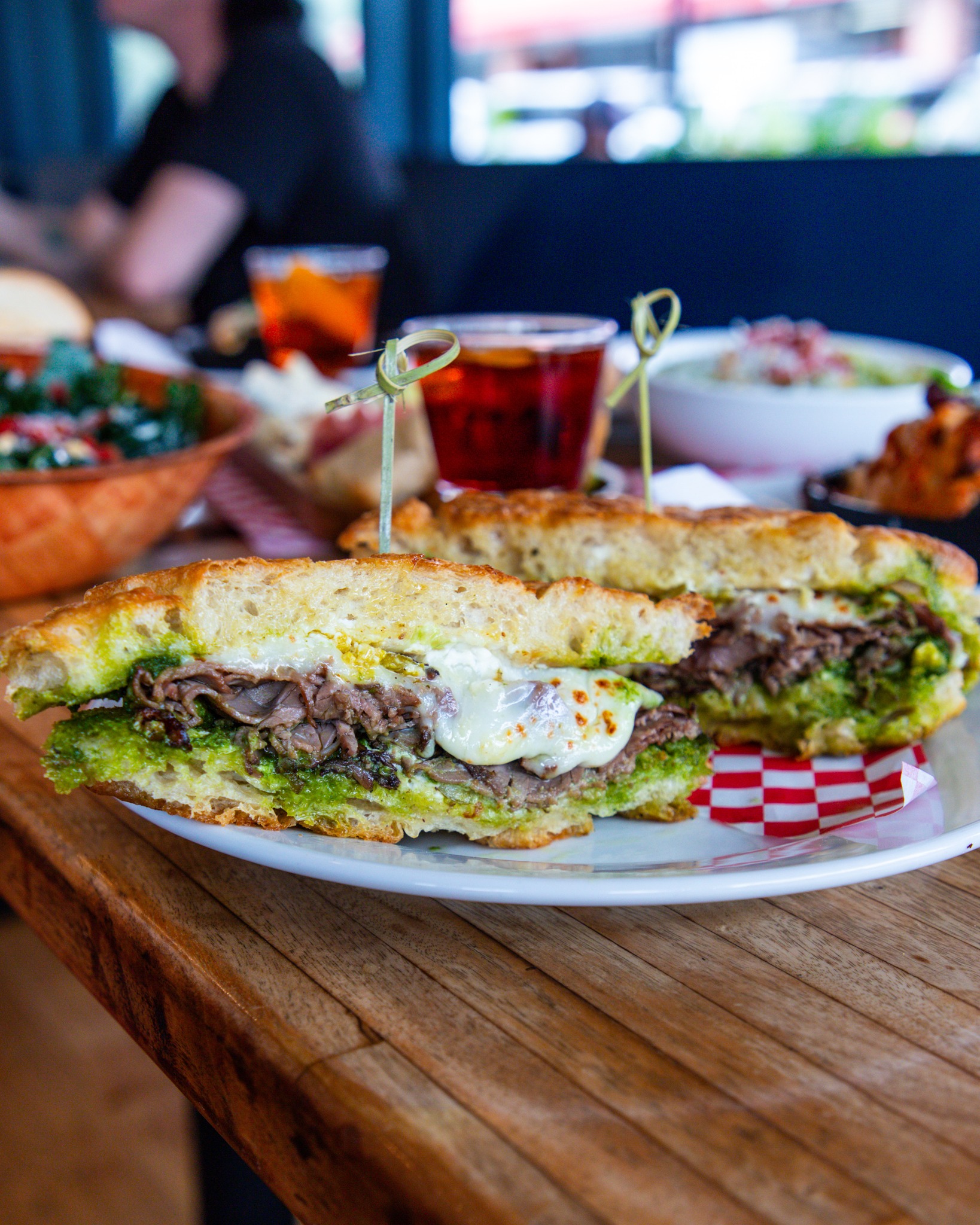 Sliced sandwich with beef, pesto, and melted cheese on a table.