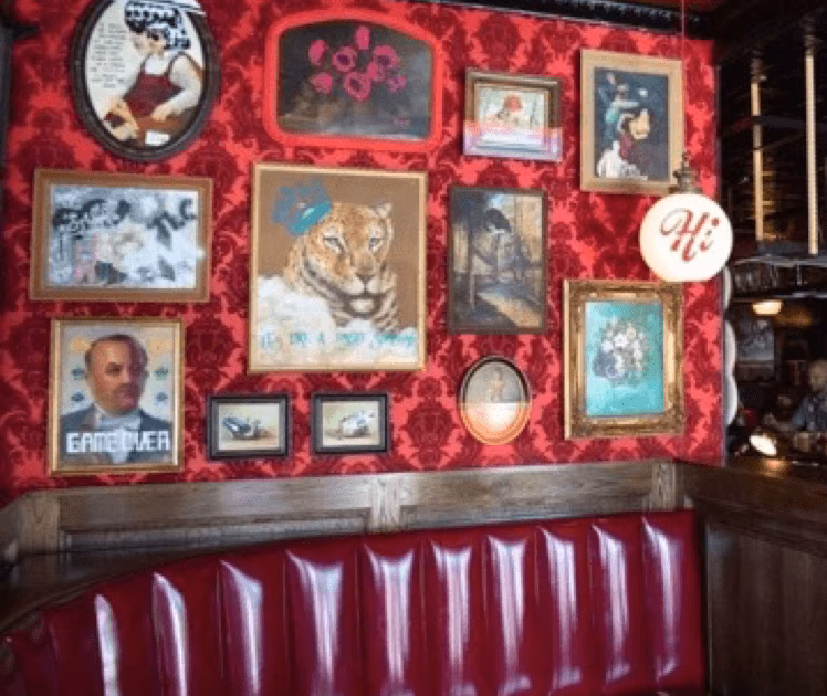 Red patterned wall covered with various framed pictures above a red booth.