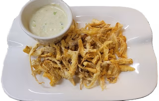 Golden fried strands on white plate with green dipping sauce.