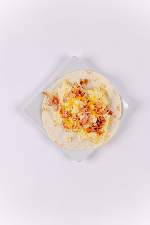 Flat tortilla with scrambled eggs, bacon, and shredded cheese.