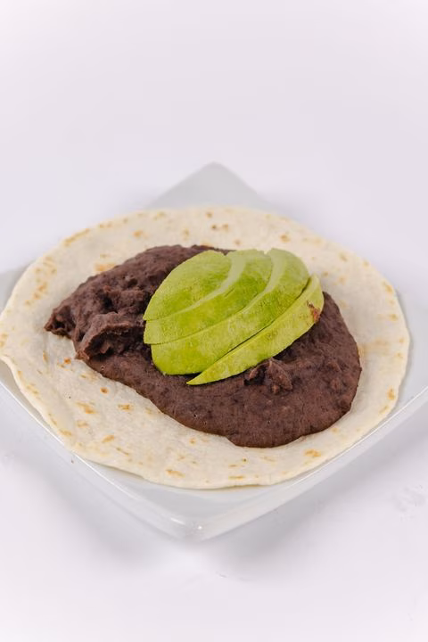 Tortilla with refried beans and avocado slices on a white plate.