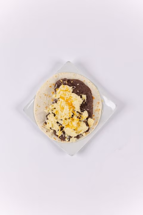 Tortilla topped with refried beans and scrambled eggs on a white plate.