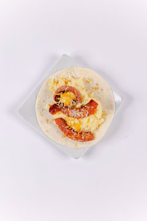 Open tortilla with scrambled eggs, sausage slices, and cheese.