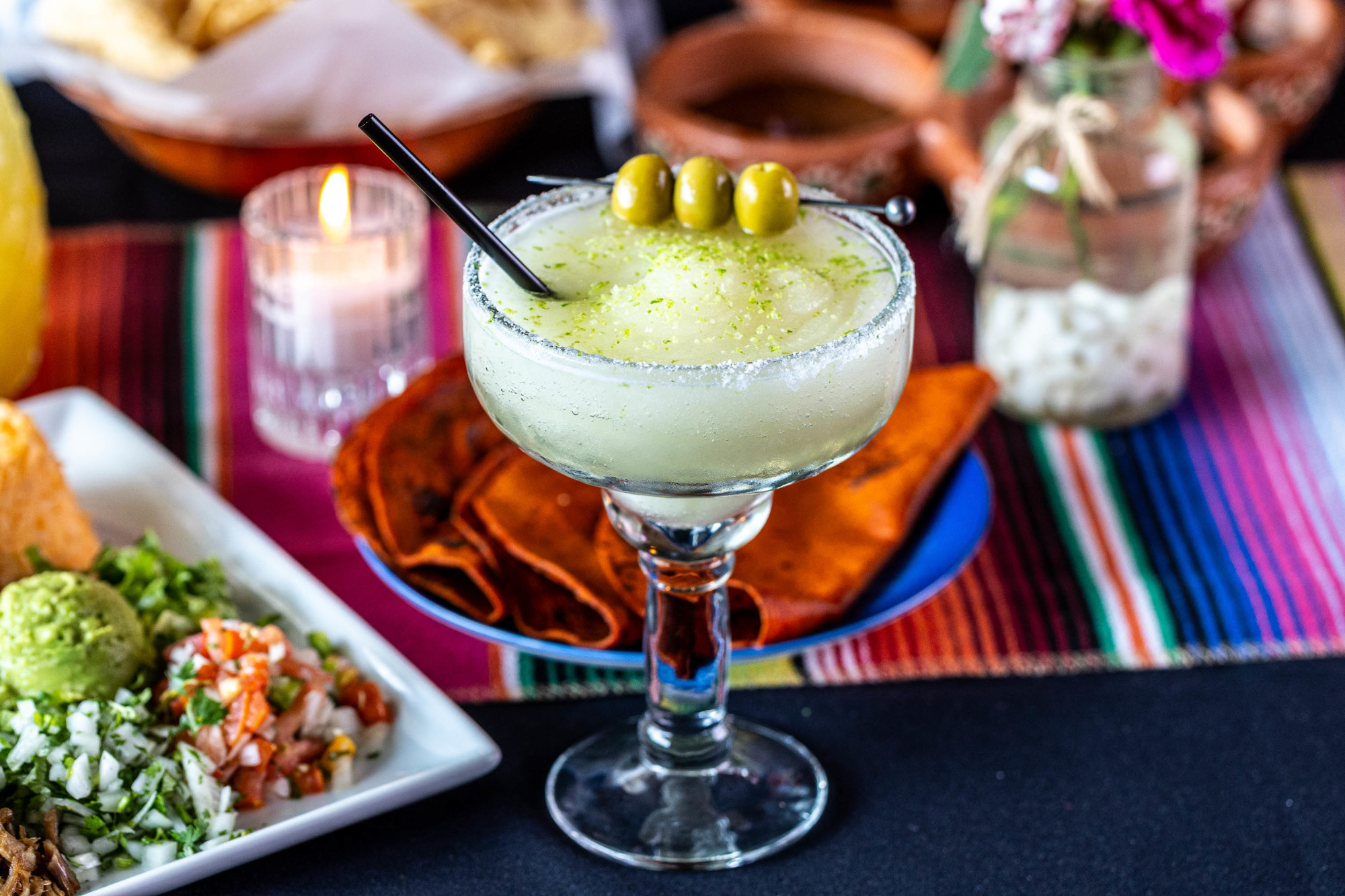 Frozen margarita garnished with olives and lime zest, with Mexican food.