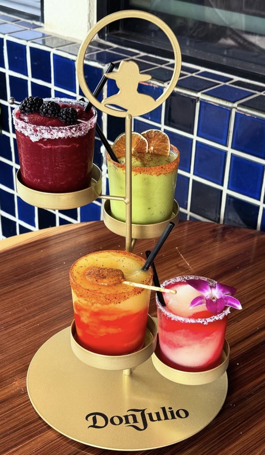 Four colorful Don Julio cocktails on a gold tiered serving stand.