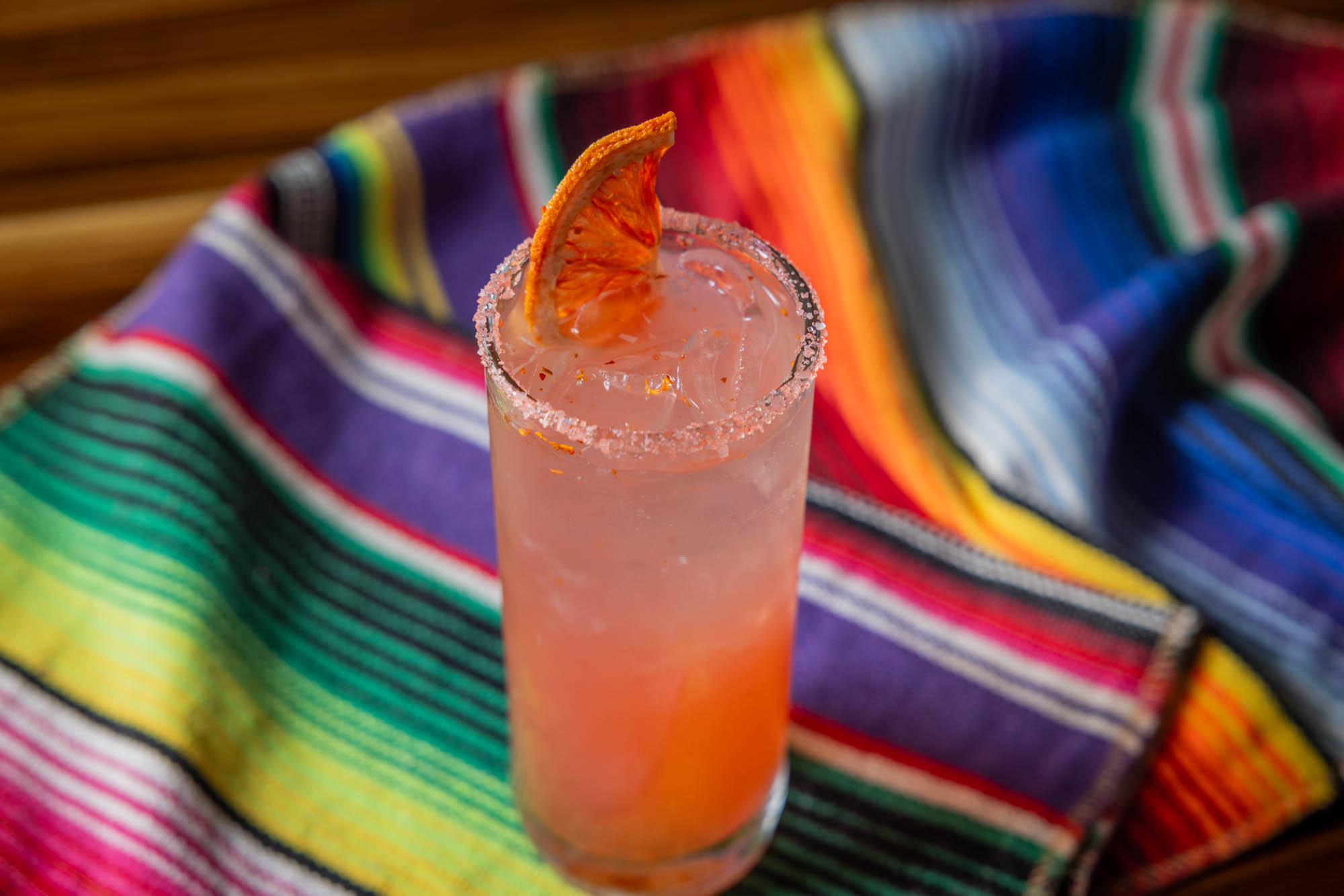 Pink drink with orange slice and sugar rim on a colorful striped blanket.
