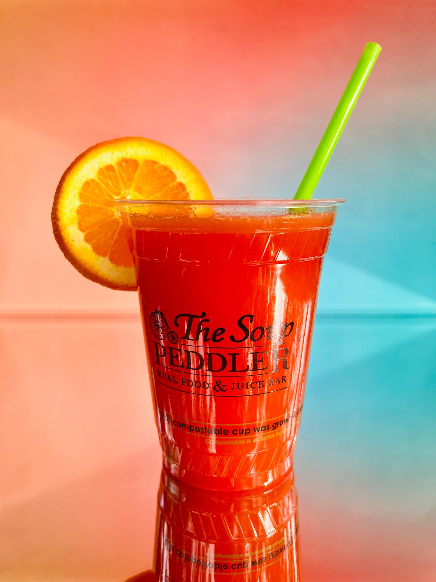 Red-orange drink in cup with orange slice and bright green straw.