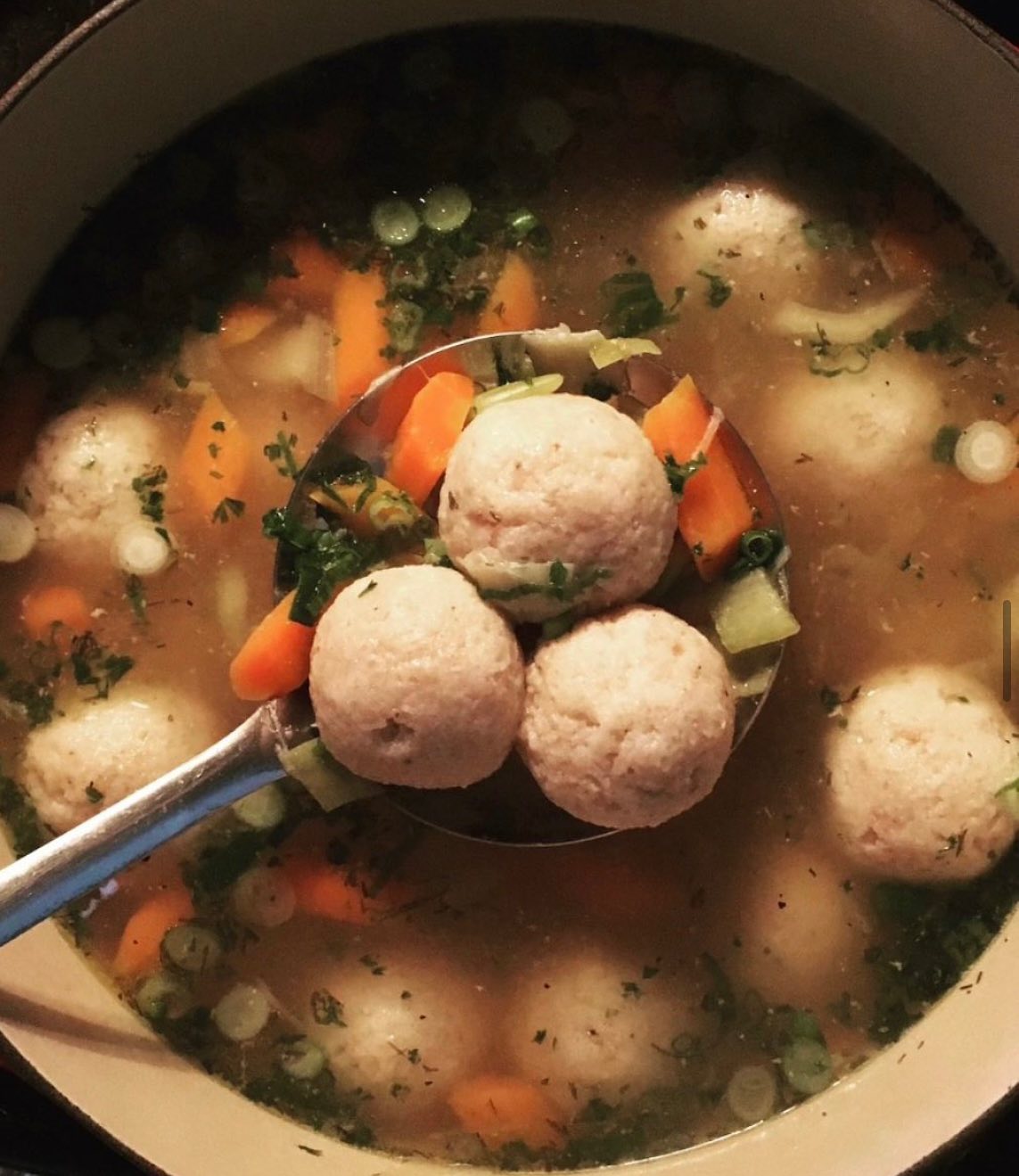 A ladle scoops three matzo balls from a pot of soup.