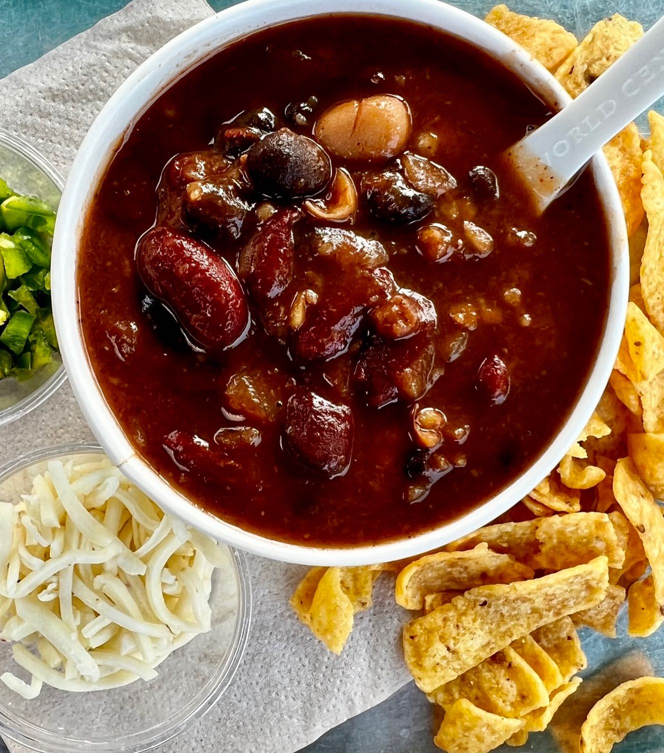 Bowl of chili with beans, shredded cheese, jalapeños, and tortilla chips.