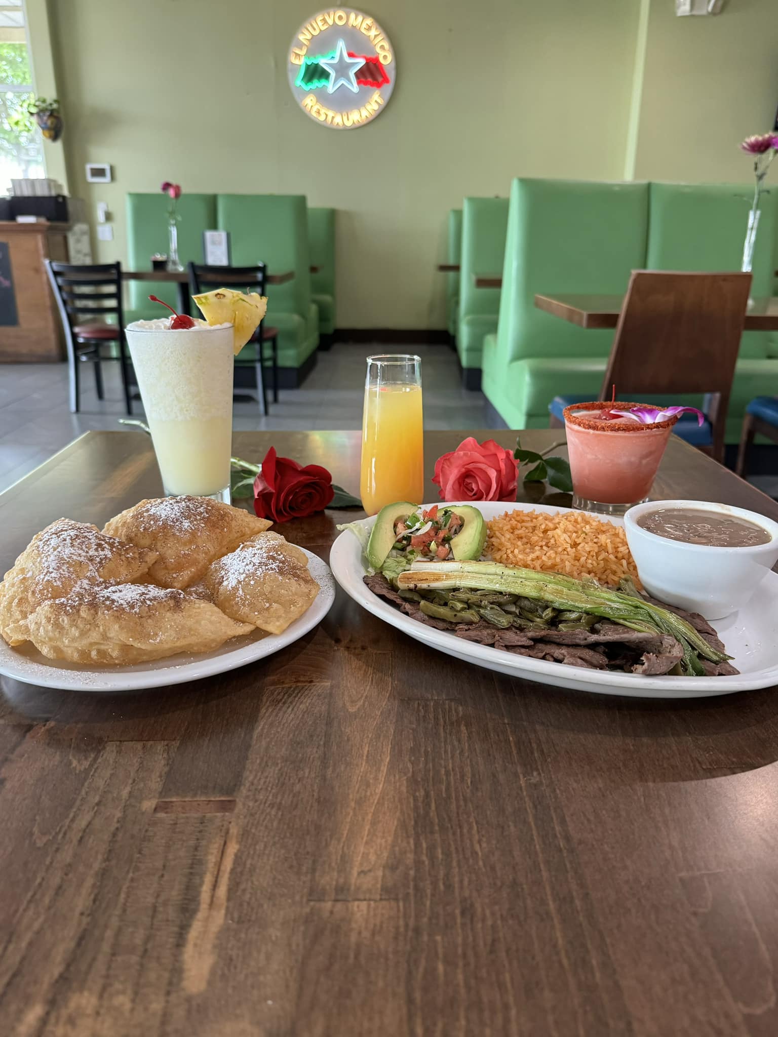 Plates of Mexican food, drinks, and roses on a restaurant table.
