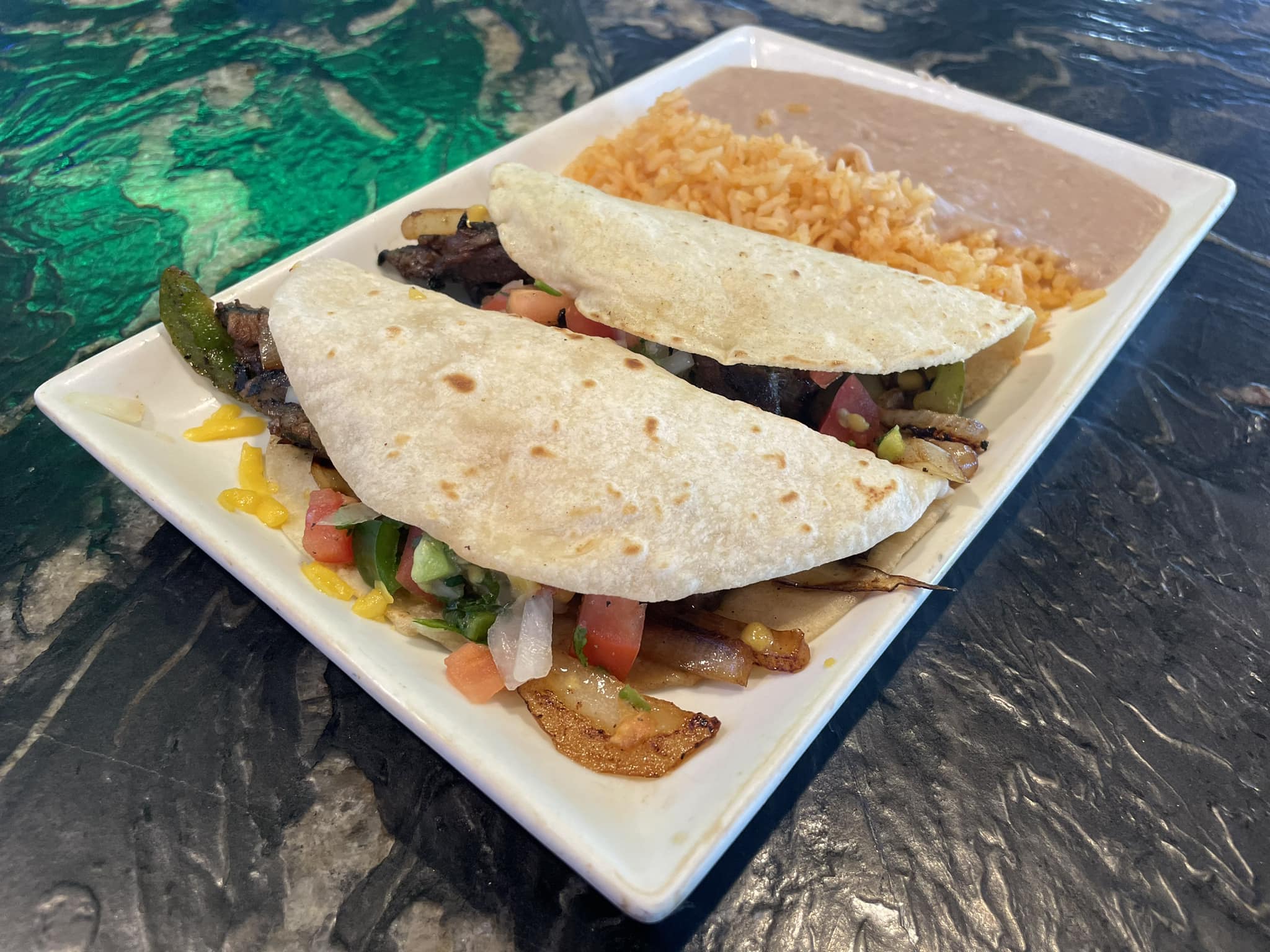Two tacos with rice and beans served on a white plate.