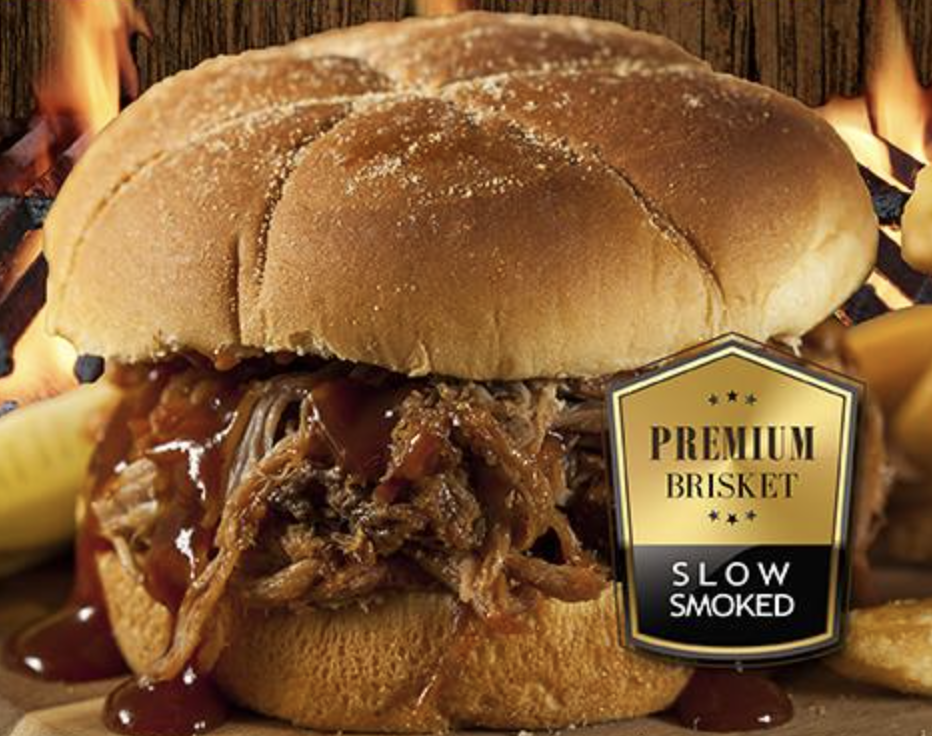 Close-up of slow-smoked pulled brisket sandwich with sauce, pickle, flames.