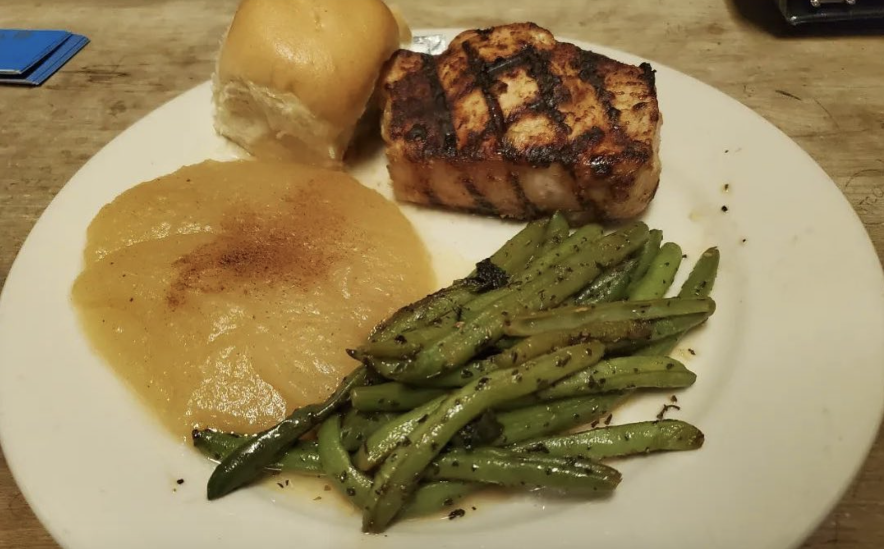 Grilled pork chop, applesauce, green beans, and a dinner roll on a plate.