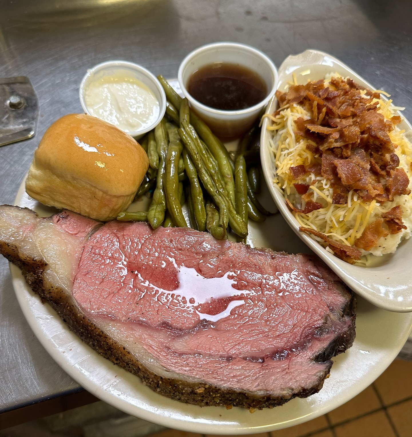 Prime rib, green beans, loaded mashed potatoes, a roll, and side sauces.