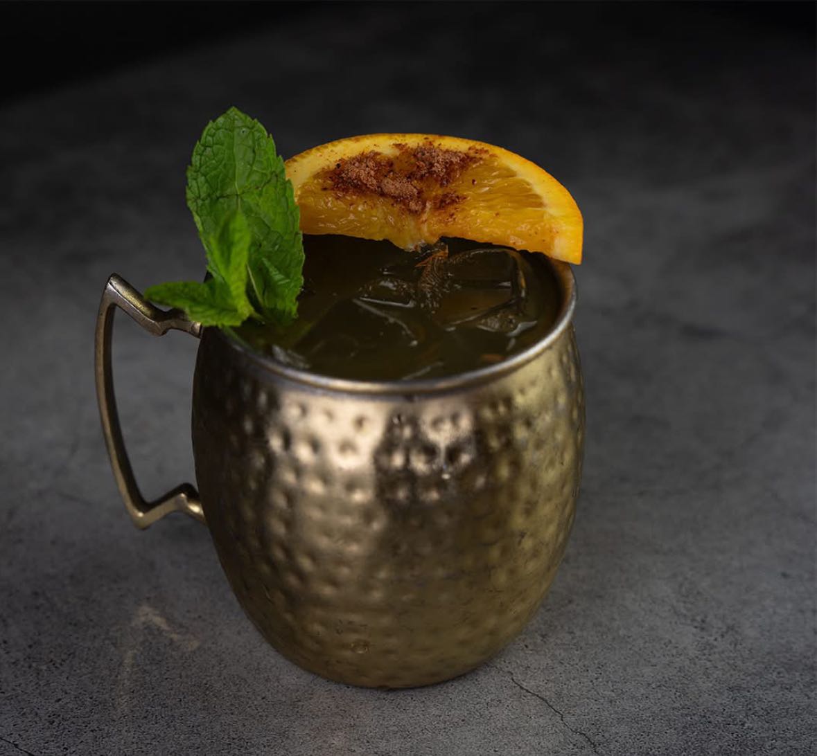 Hammered metal mug with green iced drink, mint, and orange slice.