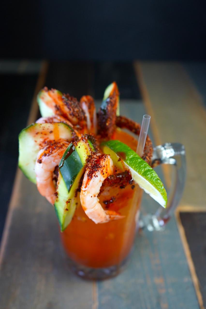 Drink with shrimp, cucumber, lime, chili powder, and a straw.