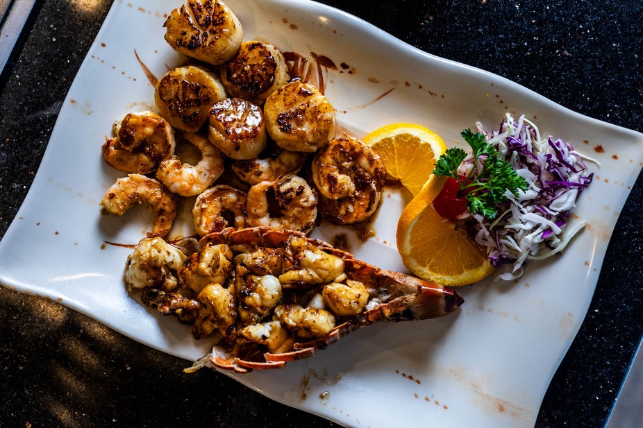 Grilled scallops, shrimp, and lobster tail with orange slices and cabbage.