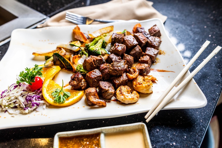 White plate with beef cubes, shrimp, mixed vegetables, and chopsticks.