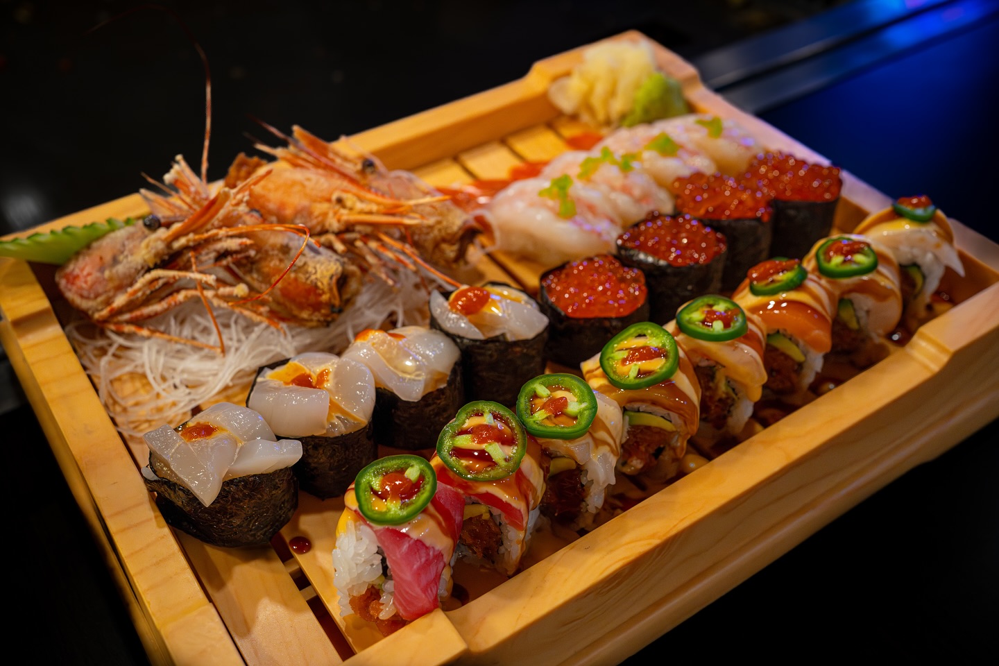 A wooden platter with assorted sushi, nigiri, and whole cooked shrimp.