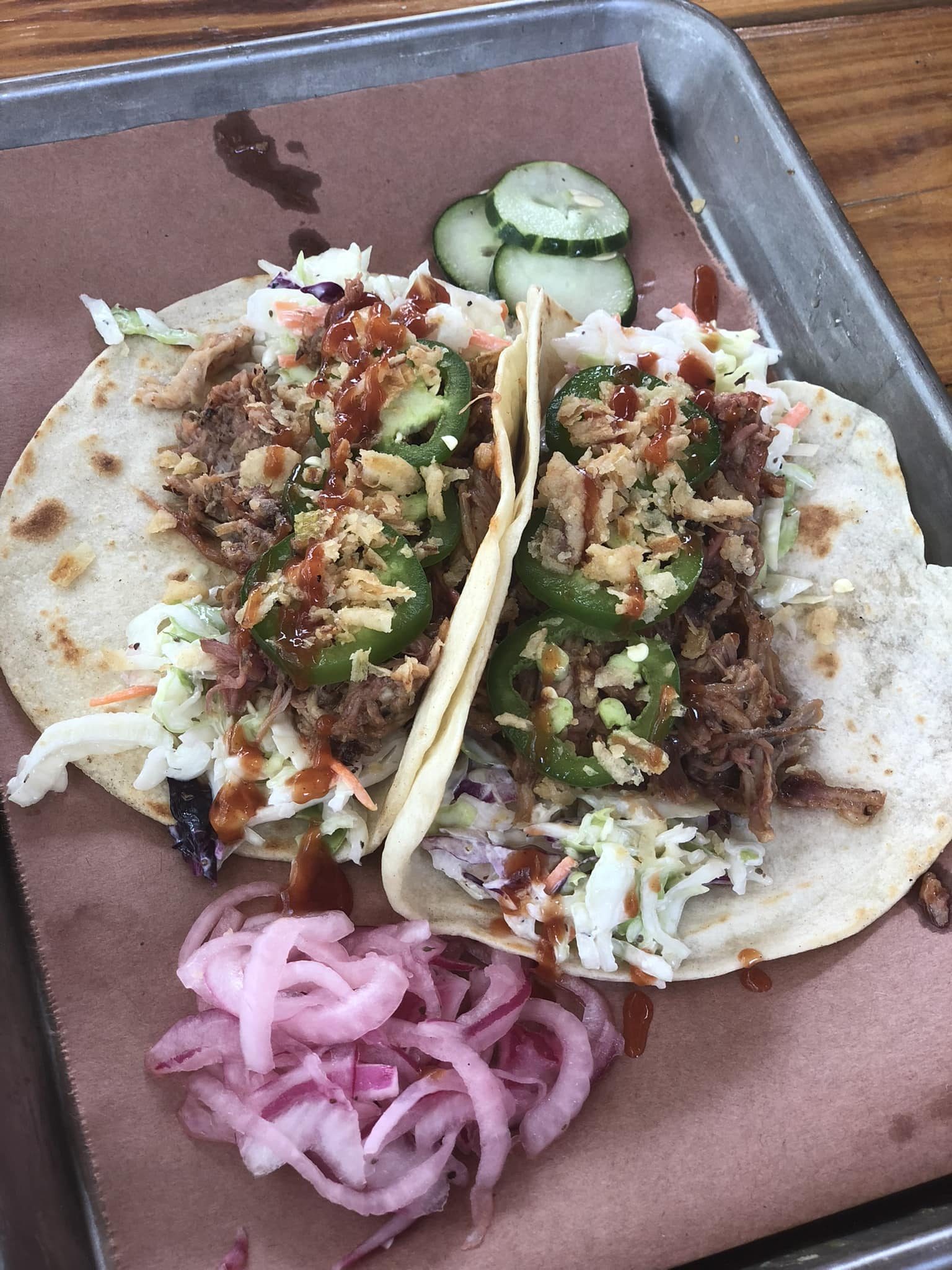 Two pulled meat tacos, coleslaw, jalapeños, pickled onions, and cucumbers.