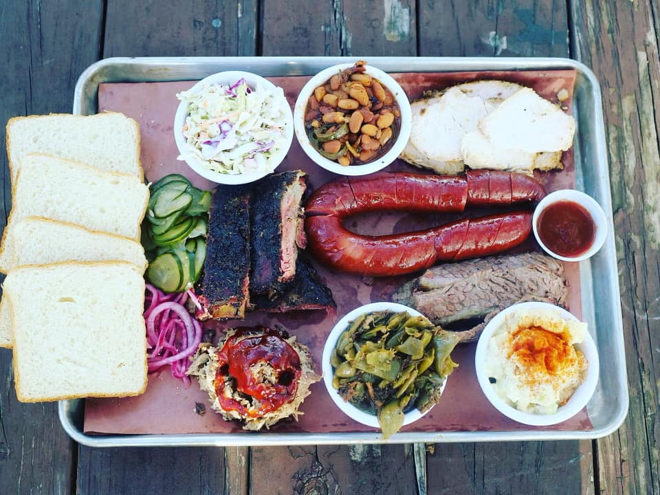 A metal tray filled with various smoked meats, sides, and white bread.