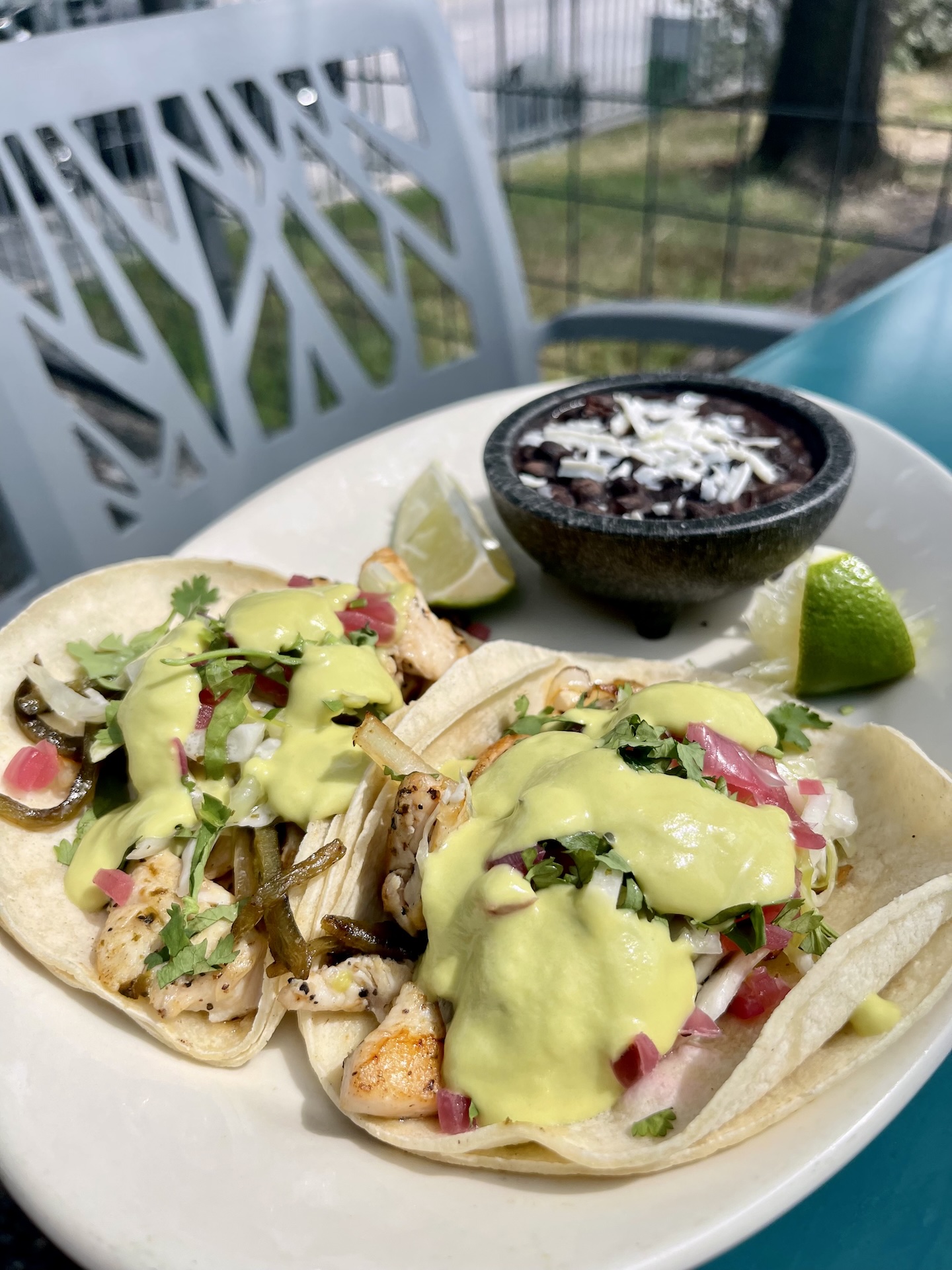 Two chicken tacos, black beans, and lime wedges on a plate.