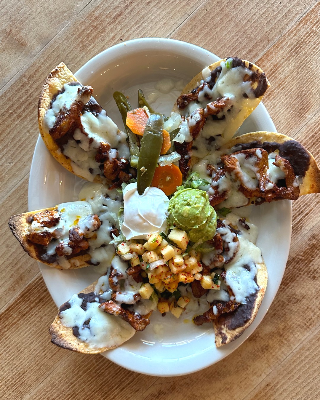 Plate of tortilla chips with cheese, meat, guacamole, salsa, and pickled vegetables.