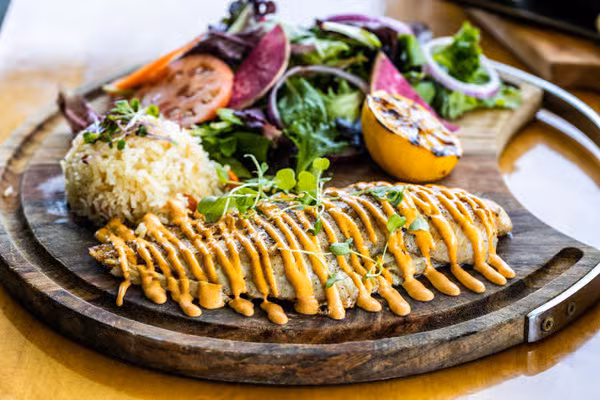 Grilled main course with rice, salad, and grilled lemon on wood.