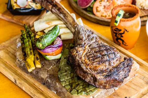 Grilled tomahawk steak with vegetables and tortillas on a wooden board.