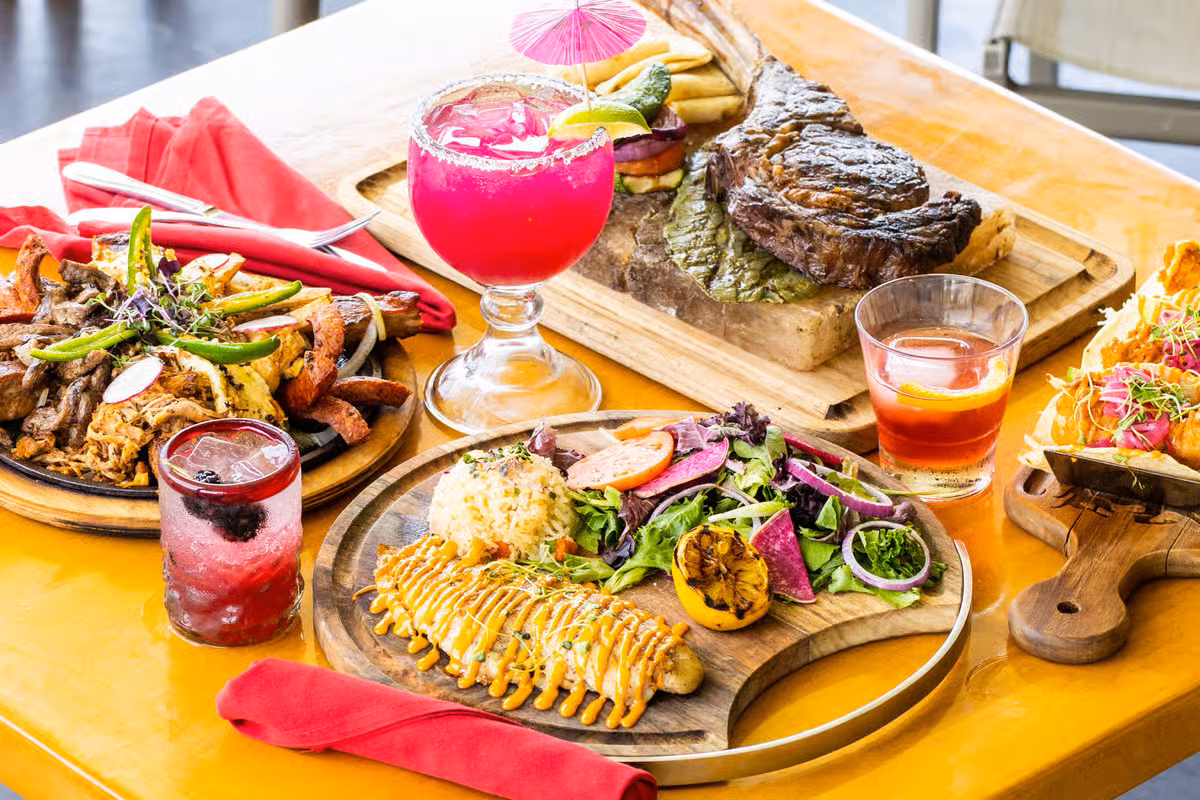 Dining table with large steak, meat platter, fish, tacos, and drinks.