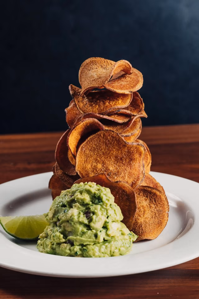 Tall stack of crispy chips with guacamole and a lime wedge.