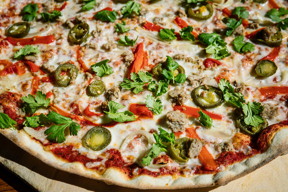 Pizza with cheese, sausage, red peppers, jalapeños, onions, and cilantro.