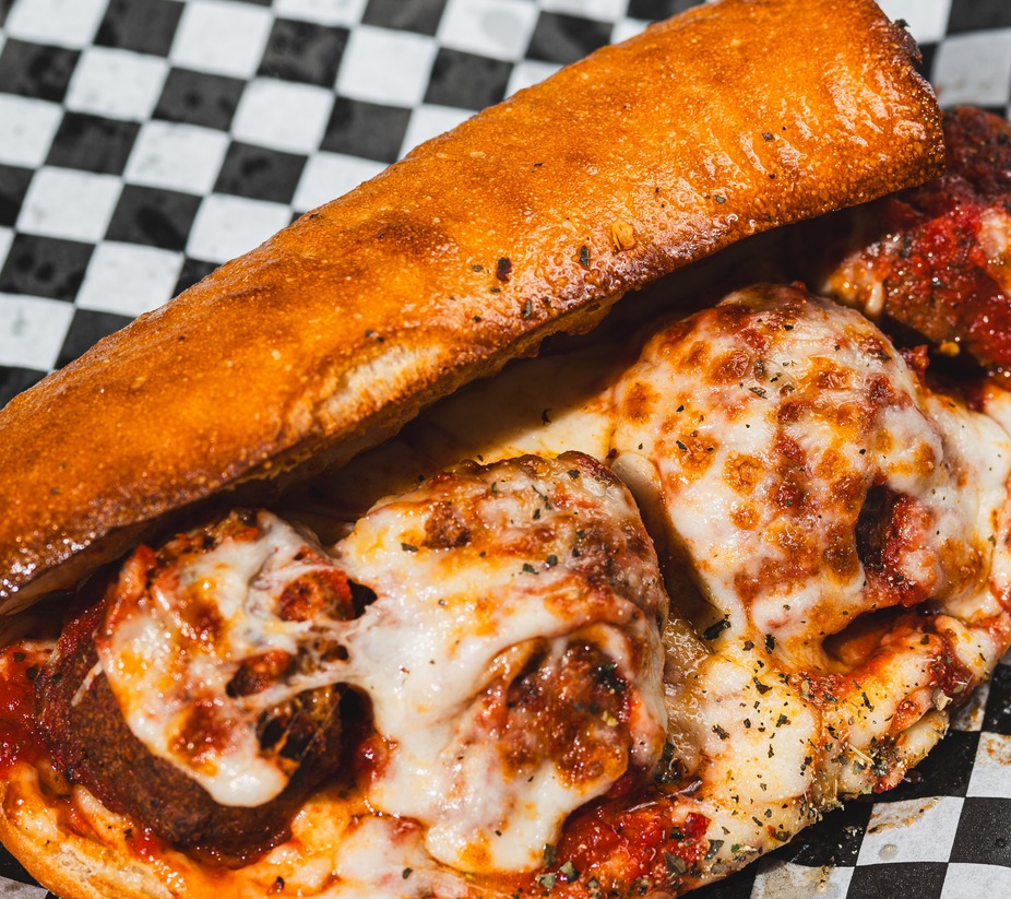 Toasted meatball sub with melted cheese, red sauce, and herbs.