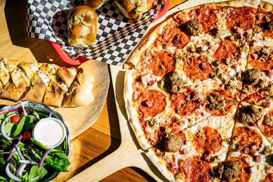 Pizza, braided cheese bread, salad, and garlic knots on a table.