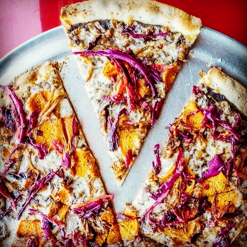 Three pizza slices with white sauce, orange vegetables, and red cabbage.