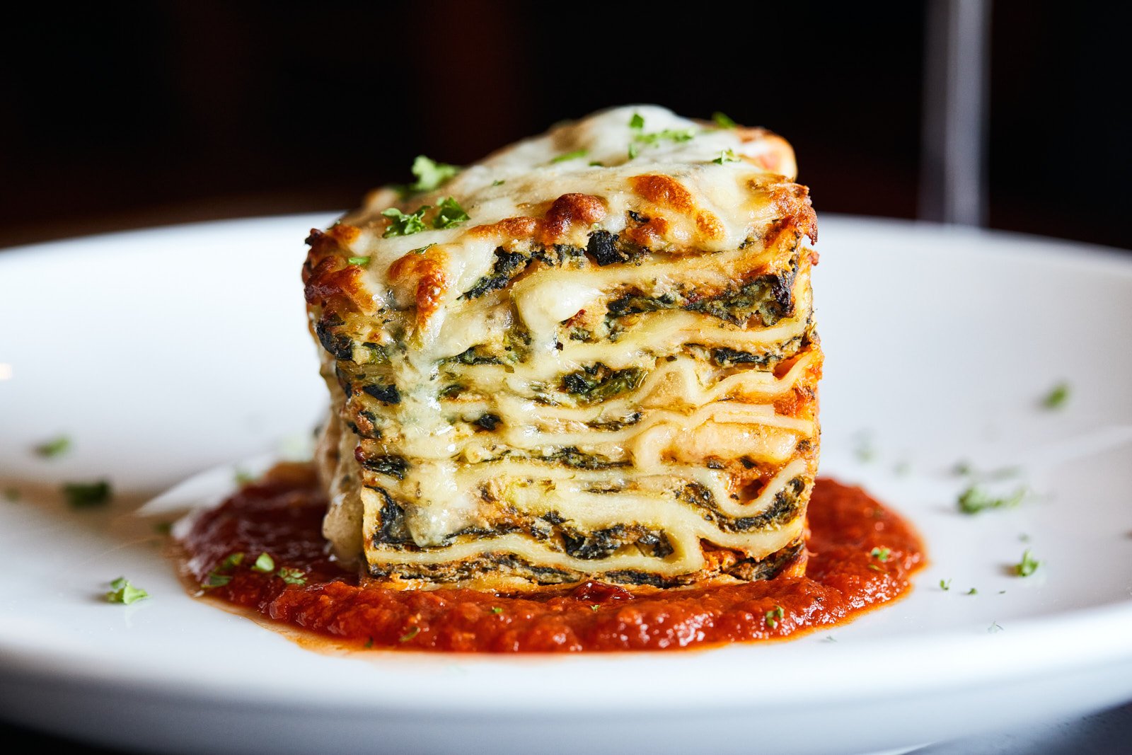 A tall slice of spinach lasagna with melted cheese and red sauce.