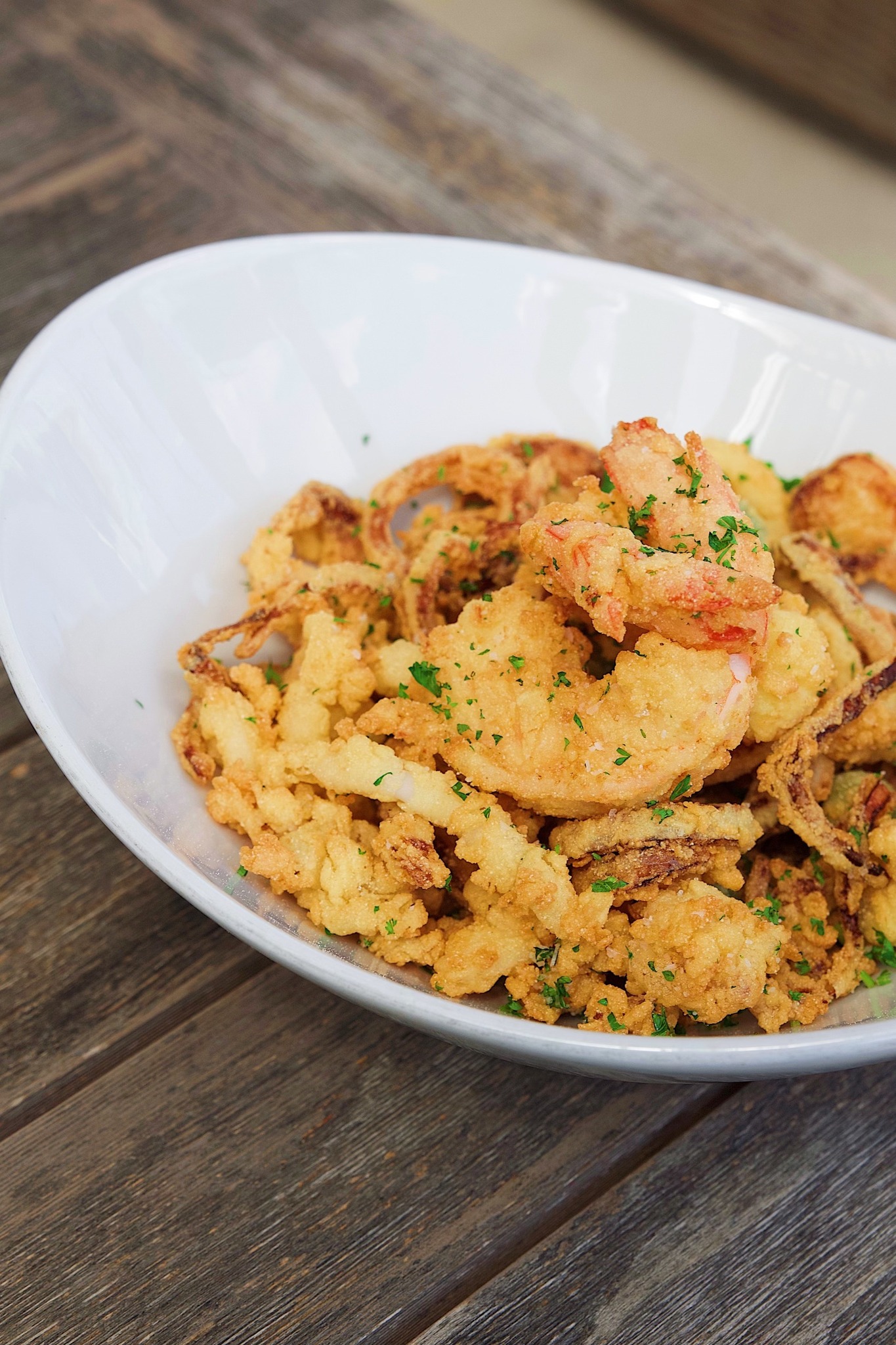 Fried shrimp, calamari, and onion rings with parsley in a white bowl.