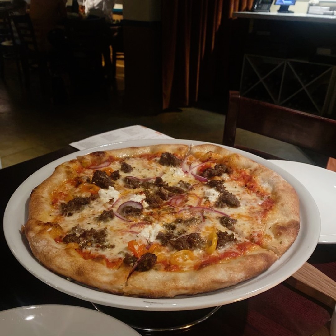 Pizza with sausage, ricotta, red onion on a white platter.