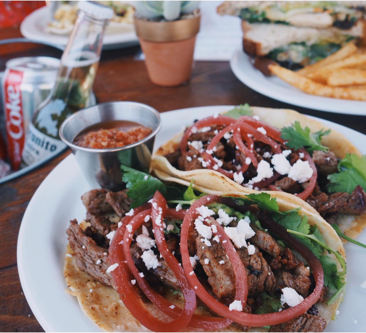 Two steak tacos with red onions, crumbled cheese, and salsa.