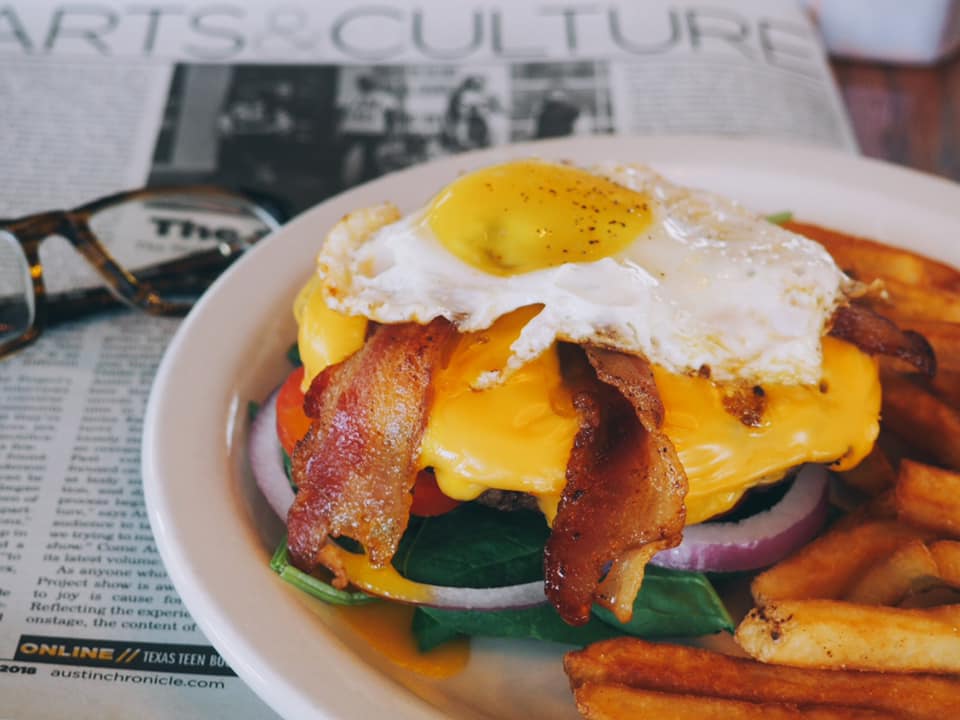 Hamburger with fried egg, bacon, cheese, and fries on a plate.