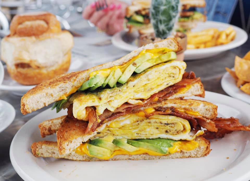 Stacked breakfast sandwich with egg, bacon, avocado, and cheese.