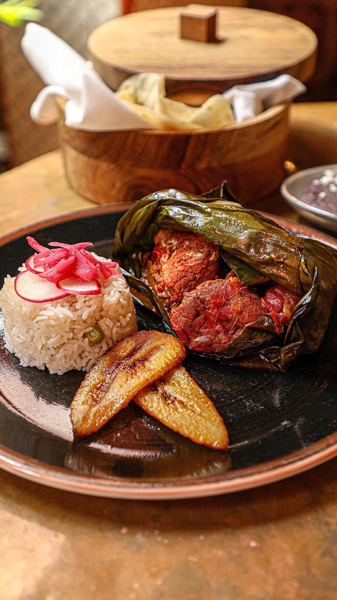Plate of rice with radish and onions, meat in leaf, plantains.