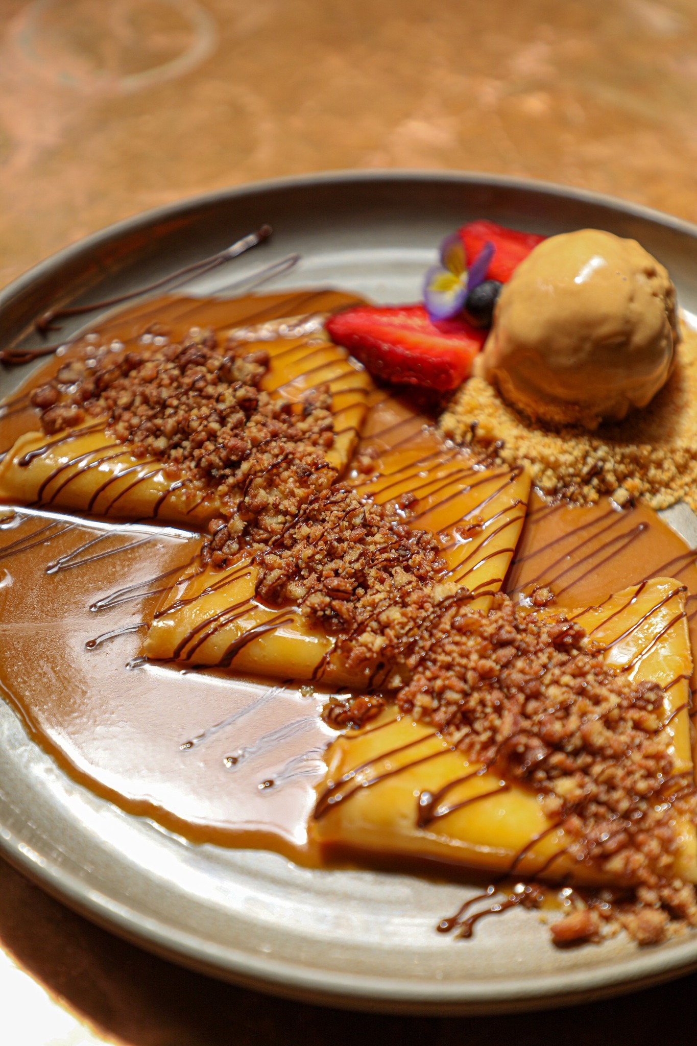 Crepes with caramel sauce, nuts, ice cream, and strawberries on a plate.