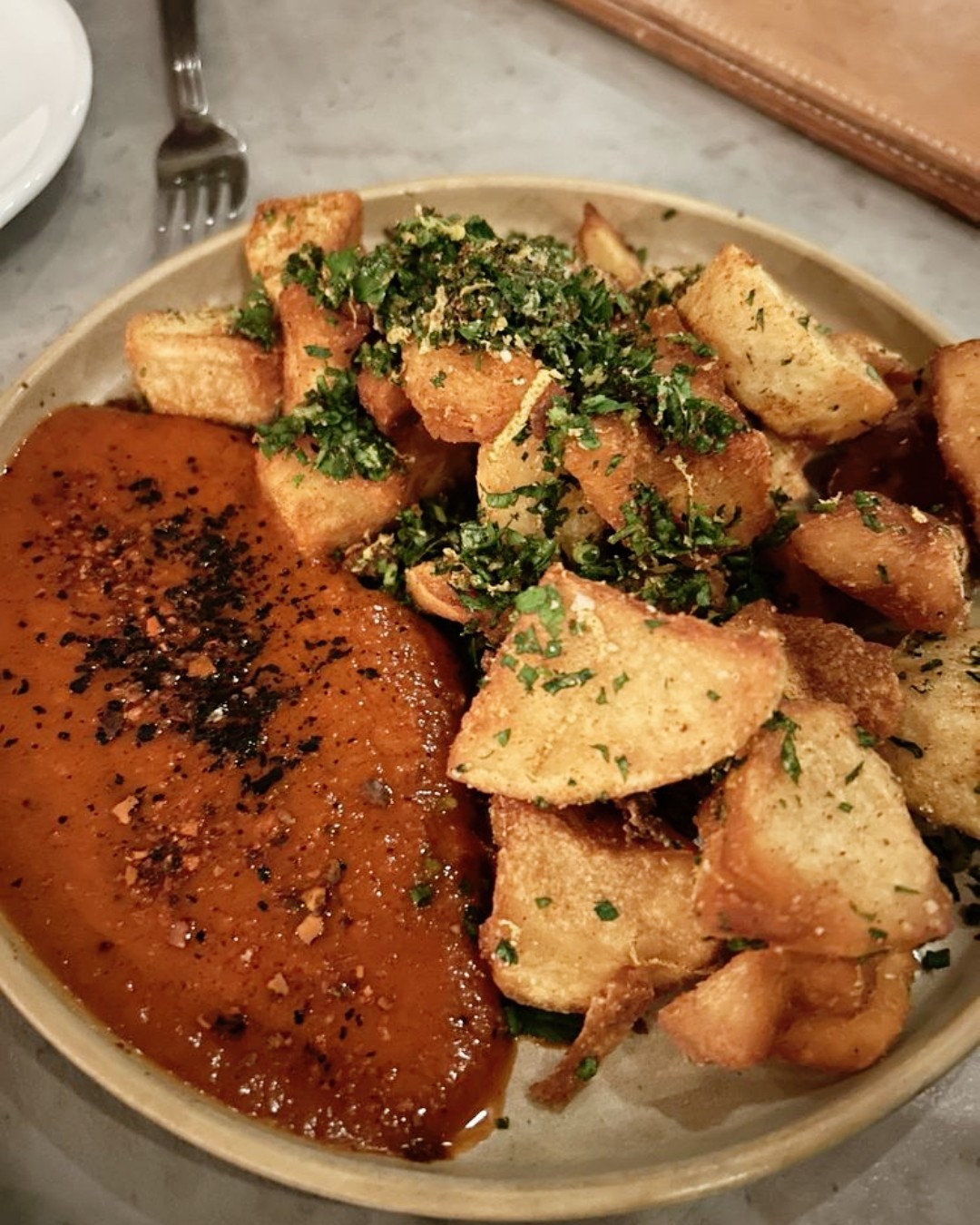Plate of fried potatoes with herbs and spiced red sauce.