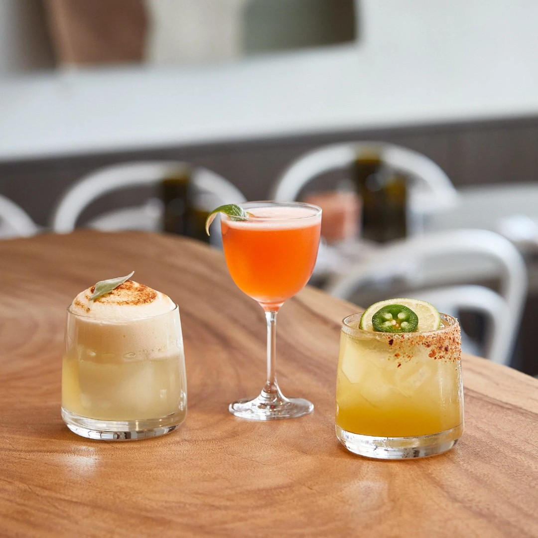 Three colorful cocktails on a wooden table.