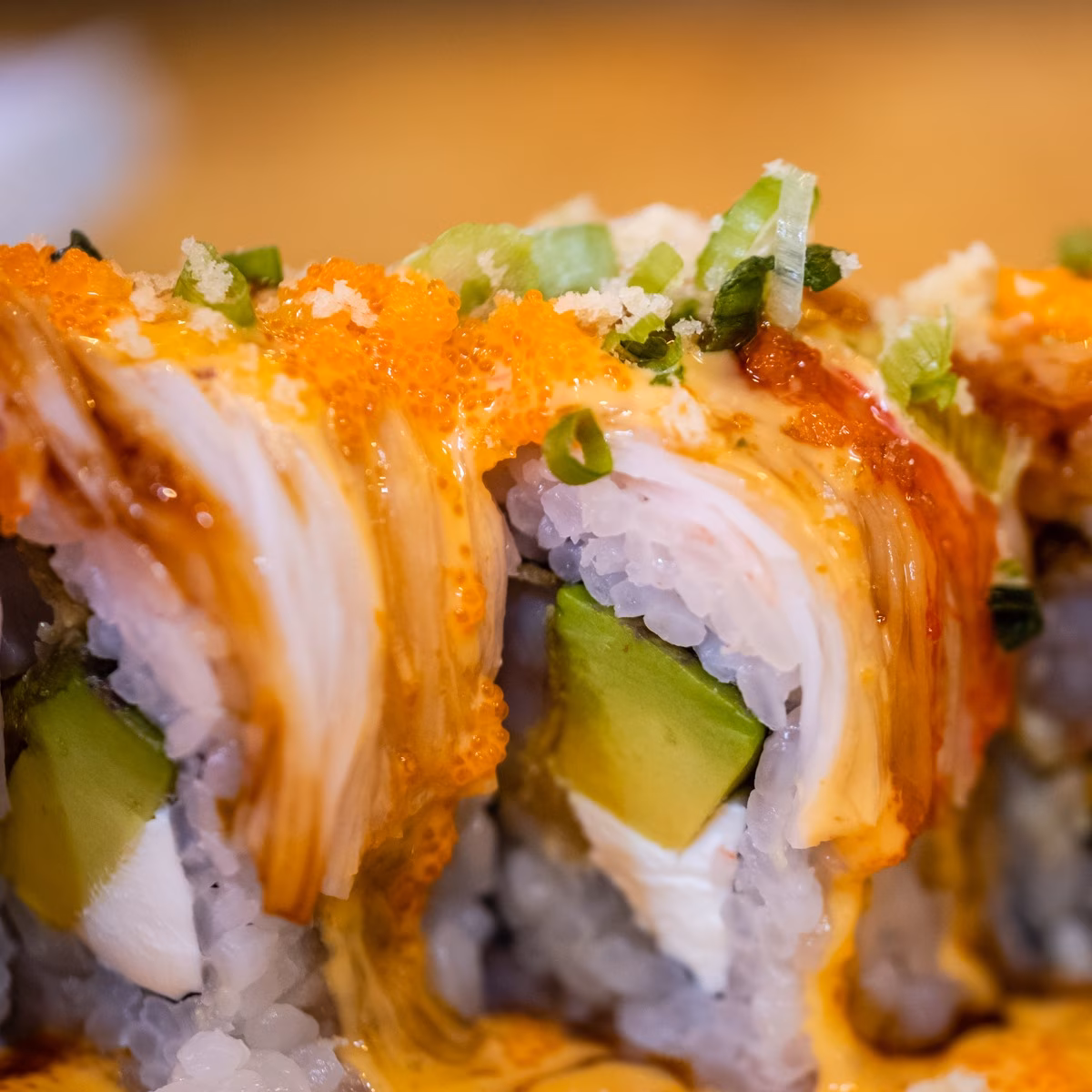 Close-up of sushi rolls topped with orange roe, sauce, and green onions.