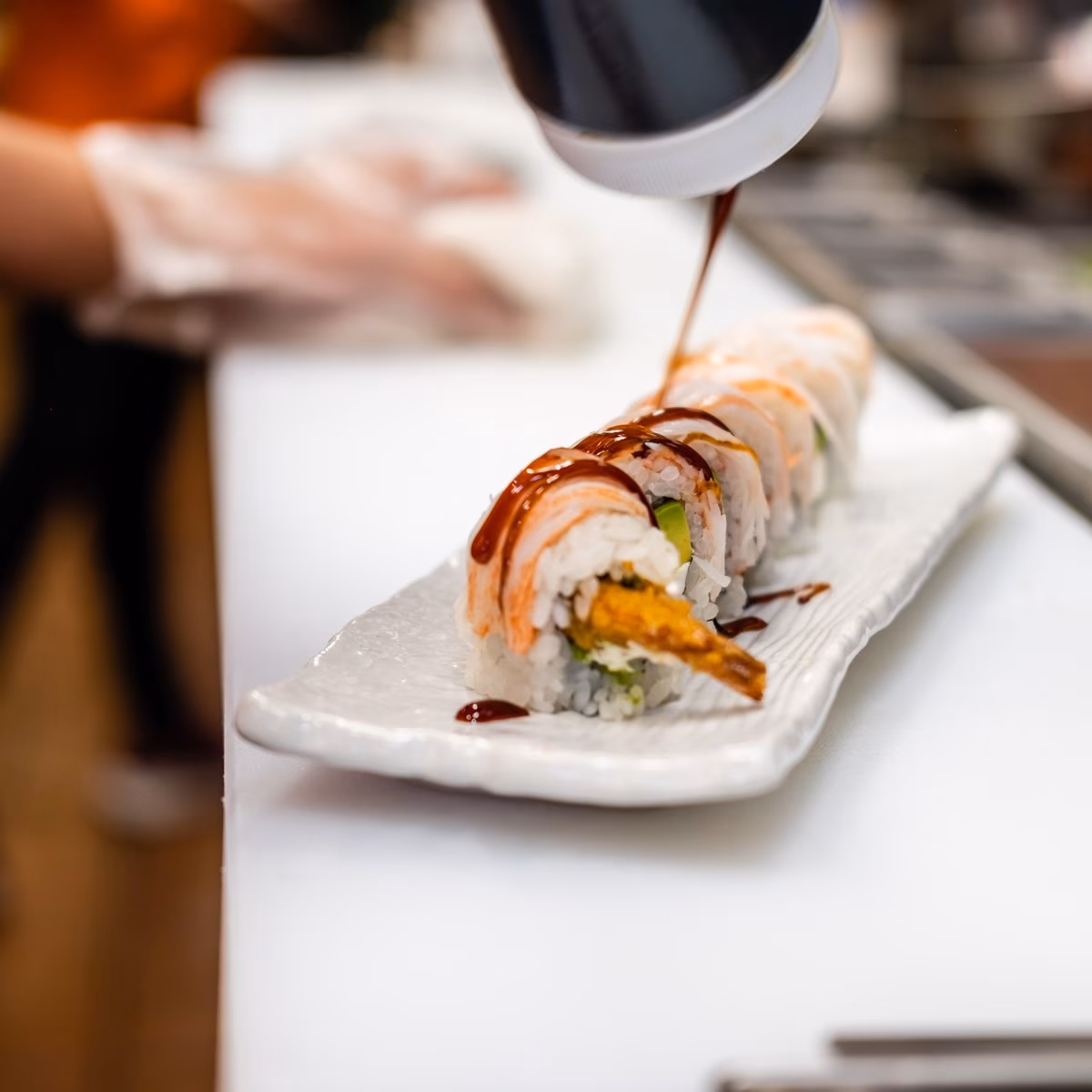 Dark sauce poured on a plate of shrimp tempura sushi rolls.